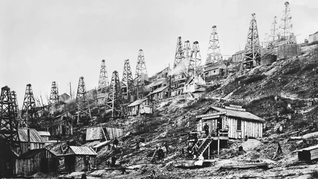 Black-and-white 1865 photo of Pioneer Run, Pennsylvania, showing dense clusters of wooden oil derricks and cabins on a steep hillside during the early oil boom.